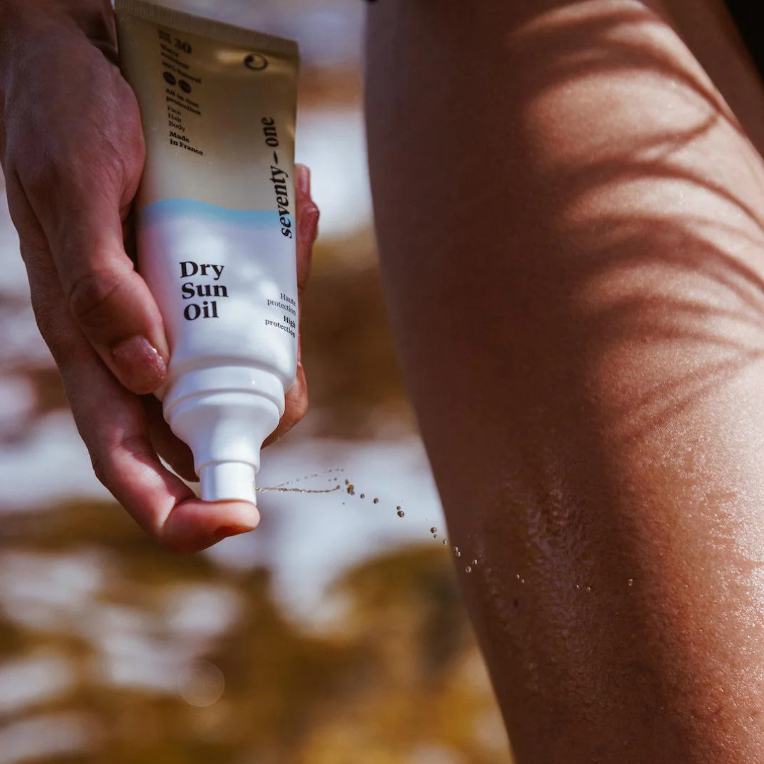 Hand applying 'Dry Sun Oil' to skin with a blurred natural background
