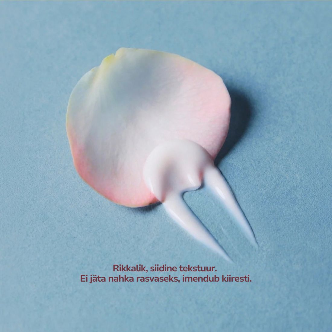 A dollop of pale pink and white cream on a textured light blue background, with a rose petal shape behind it and small Finnish text near the bottom.