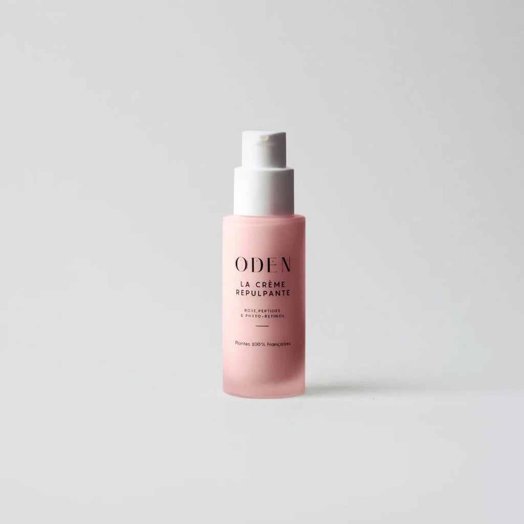 A pink cosmetic pump bottle with a white pump dispenser, featuring the brand name 'ODEN' and product name 'LA CRÊME REPULSANTE' printed on the front, set against a clean light gray background.
