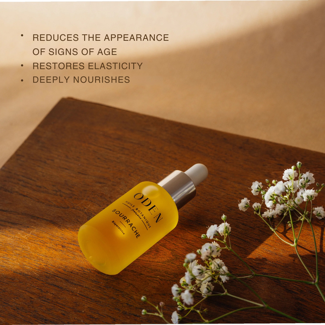 Yellow serum bottle on a wooden surface with flowers, text about product benefits.