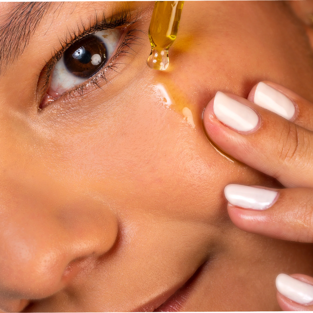 Close-up of a woman applying a dropper of oil to her skin.