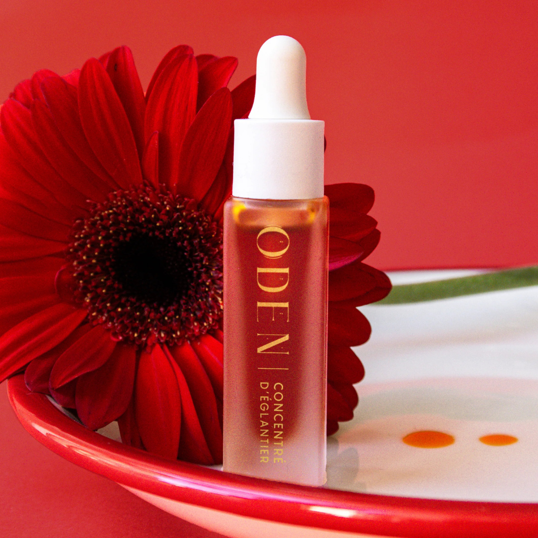 Skincare dropper bottle with red flower on a red background