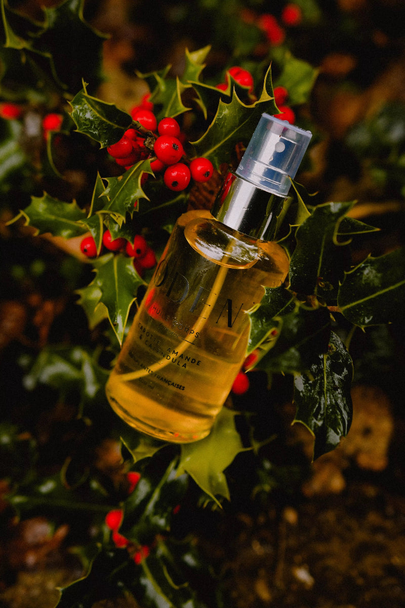 Bottle of oil with a spray cap on a background of green leaves and red berries