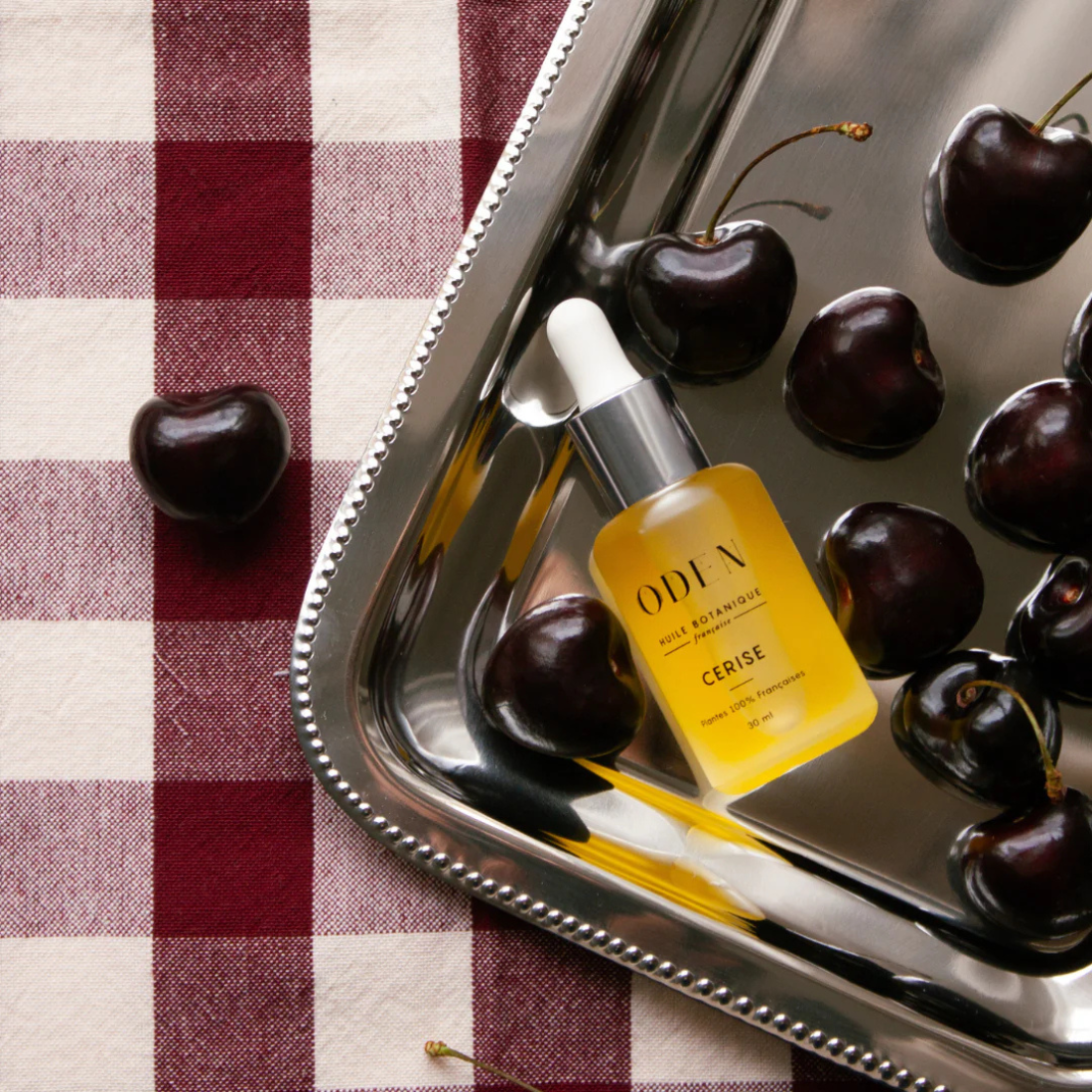 ODEN skincare serum bottle with cherries on a checkered tablecloth