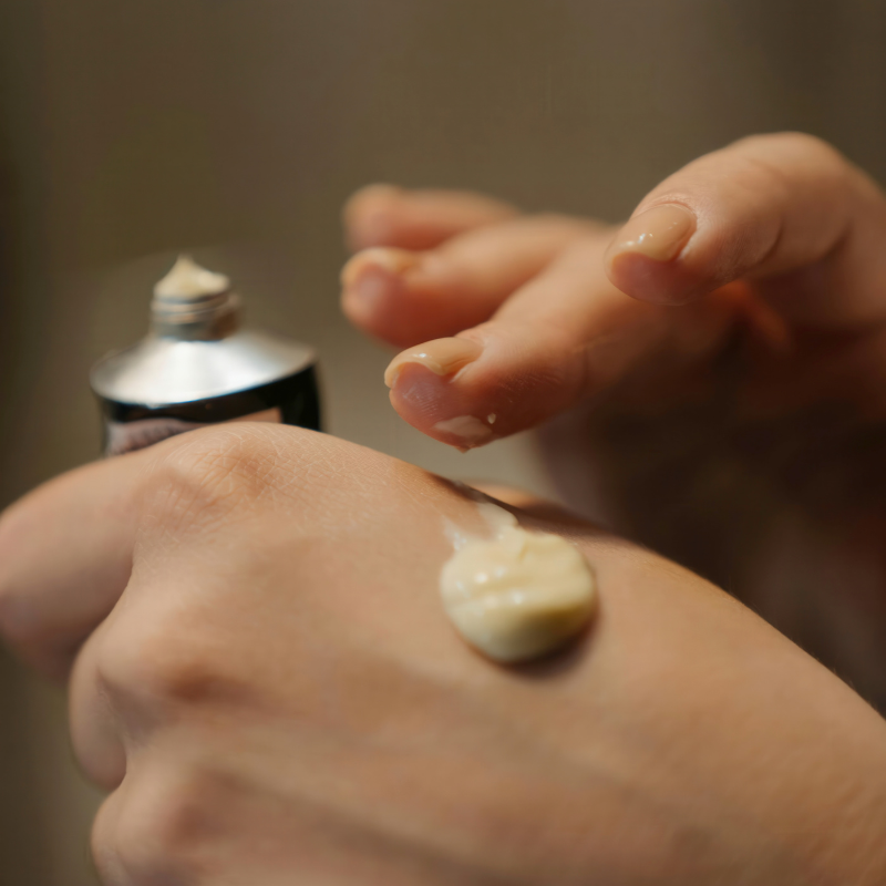Person applying cream to their hand with a focus on the cream and hand.