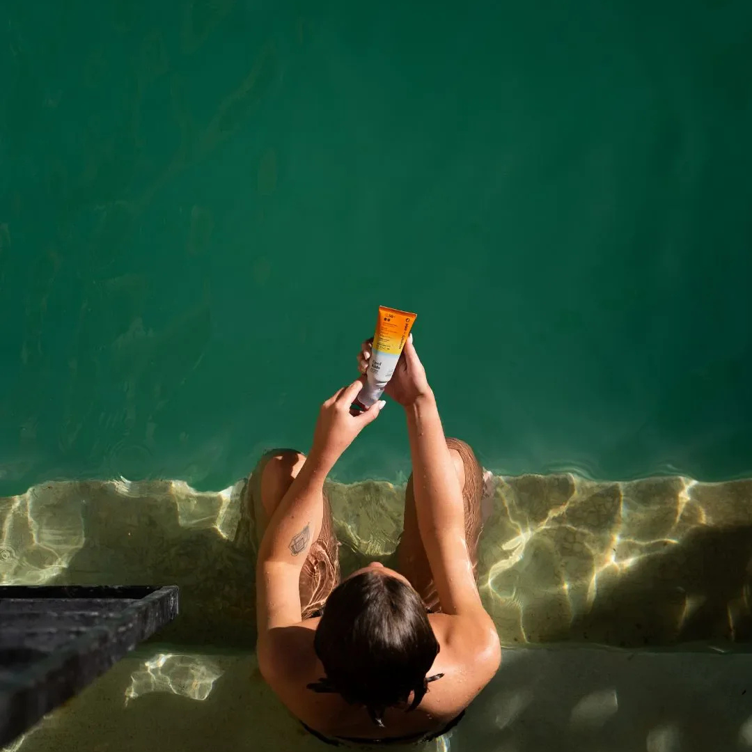 Person in a pool holding a sunscreen tube above water - sun_kissed_lotion_spf50