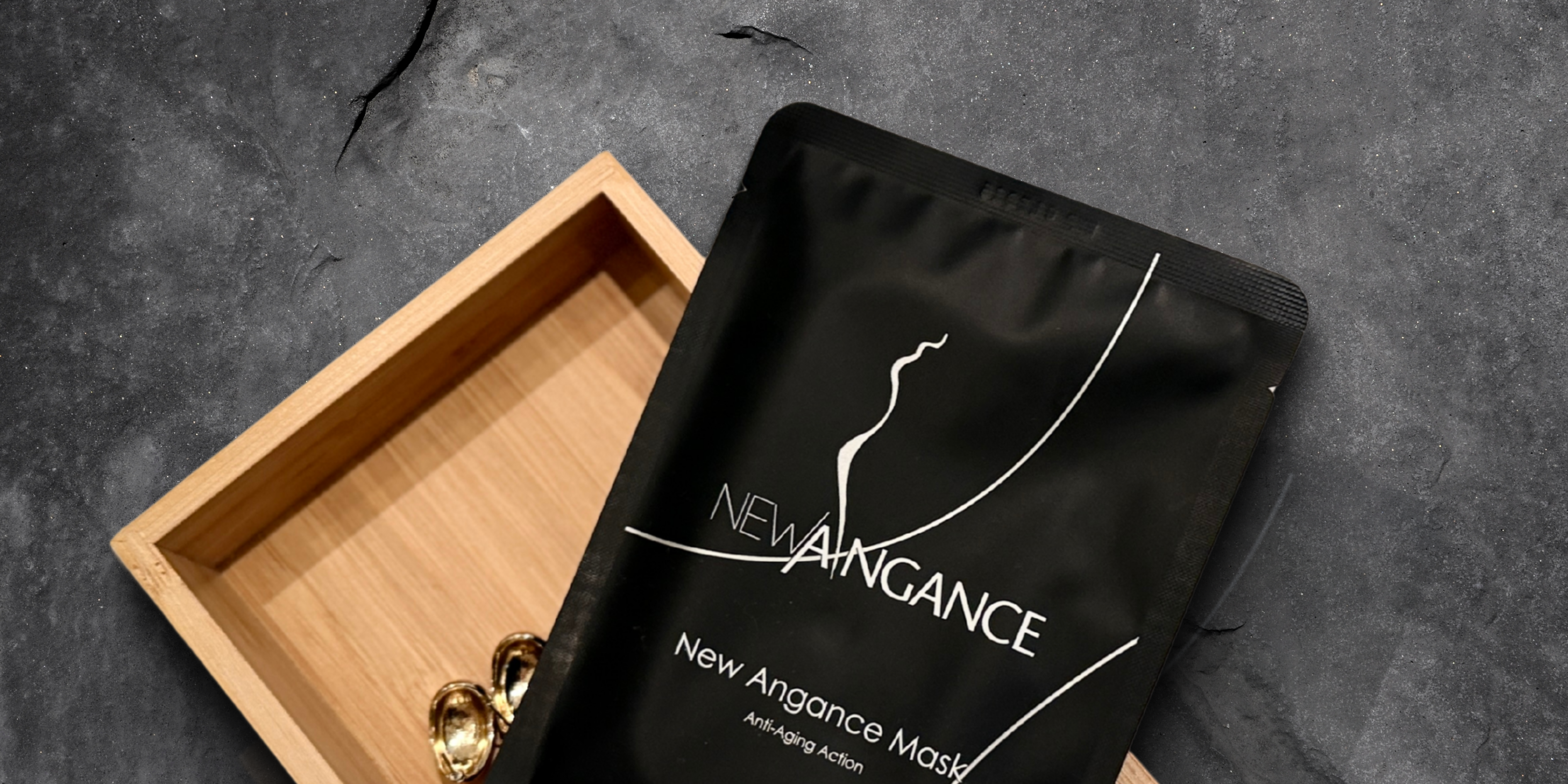 Black New Angance mask packaging on a gray surface with a wooden tray.