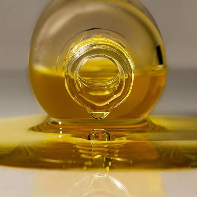 Close-up of a bottle cap with yellow liquid spilling out on a reflective surface.